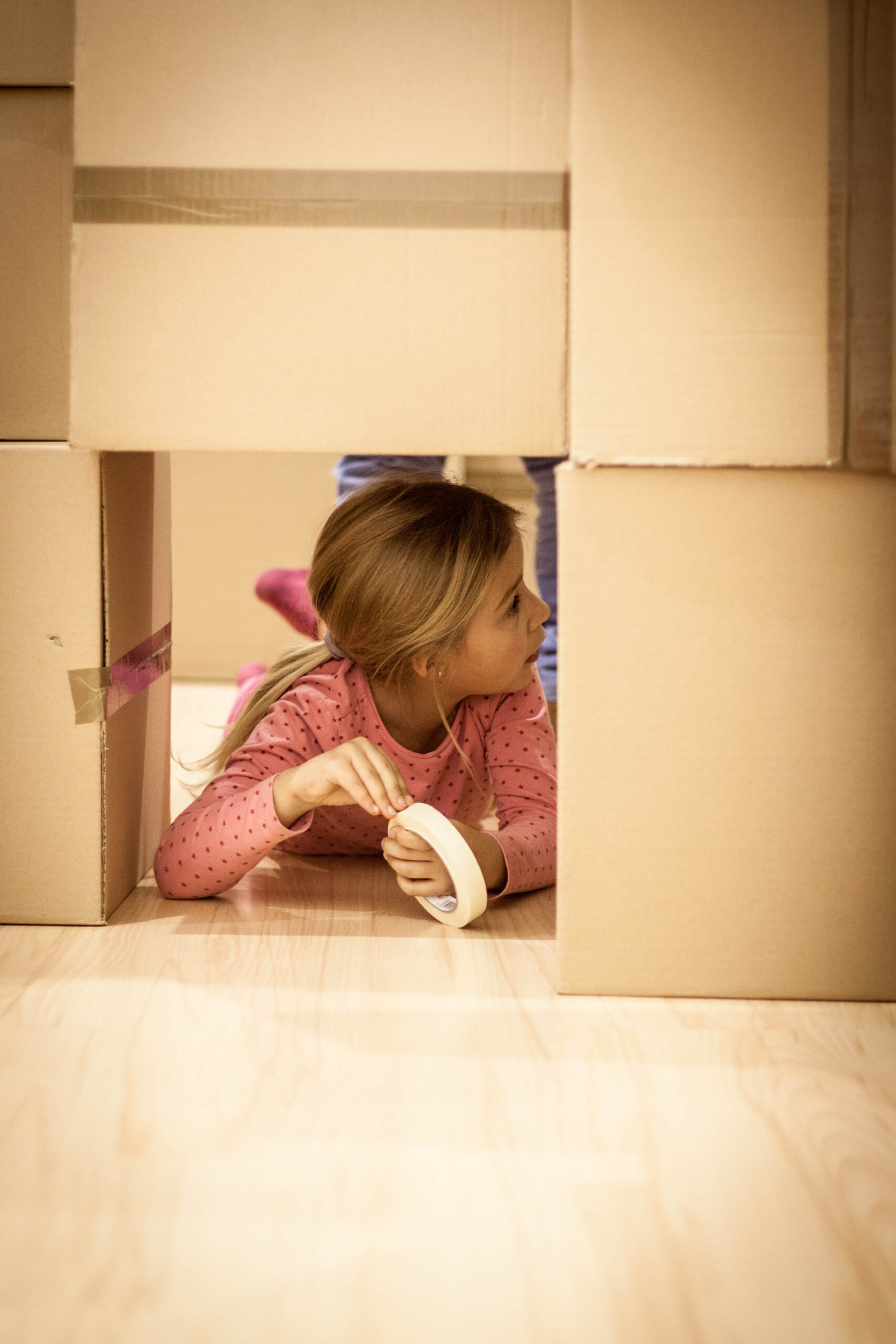 Niña asomándose por un hueco entre cajas.