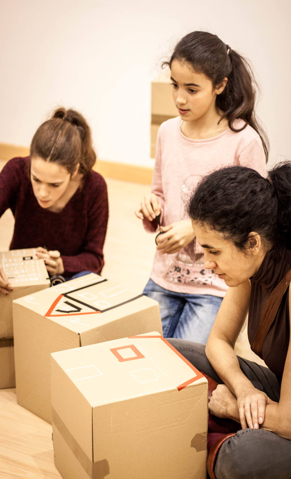 Personas adultas y niñas decorando cajas de cartón.