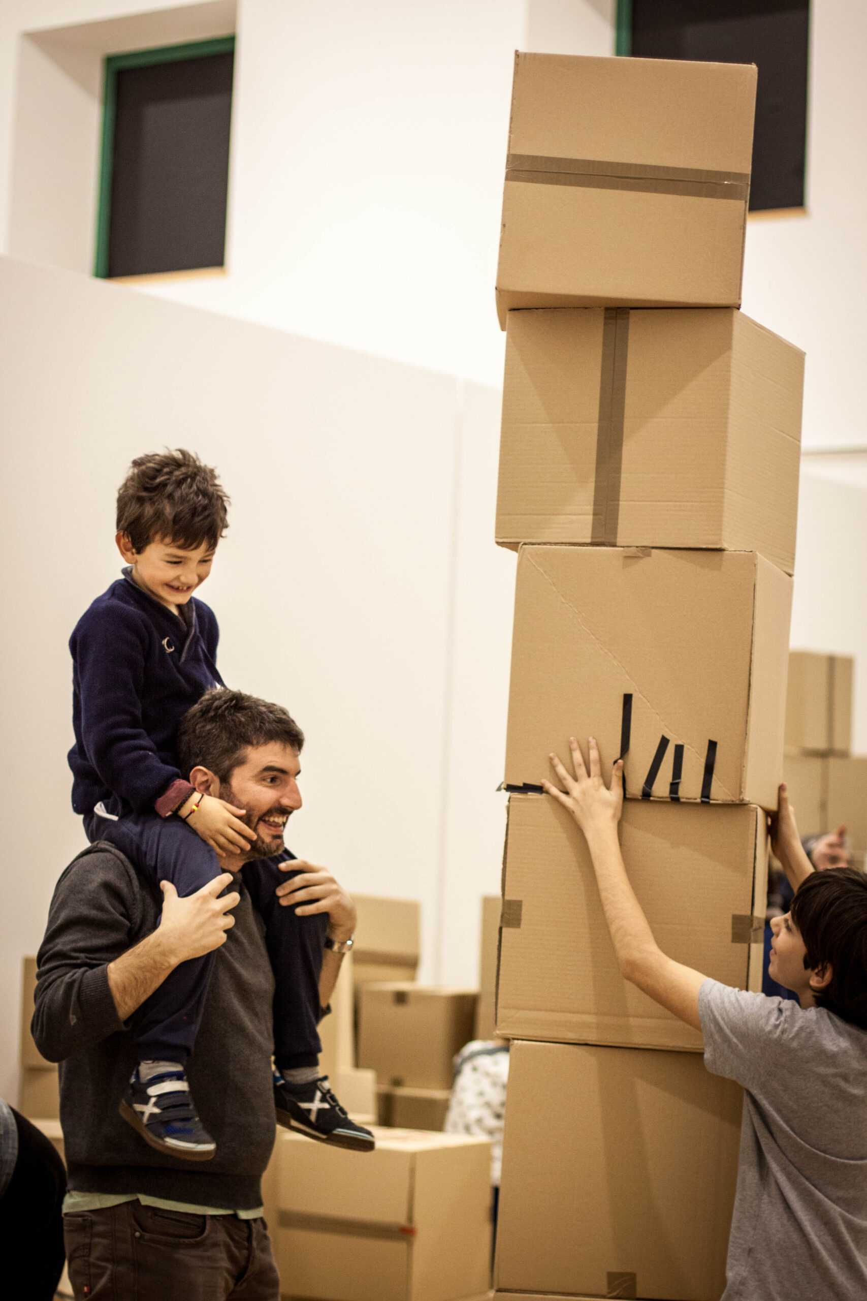 Niño sobre los hombros de un adulto junto a una torre de cajas.