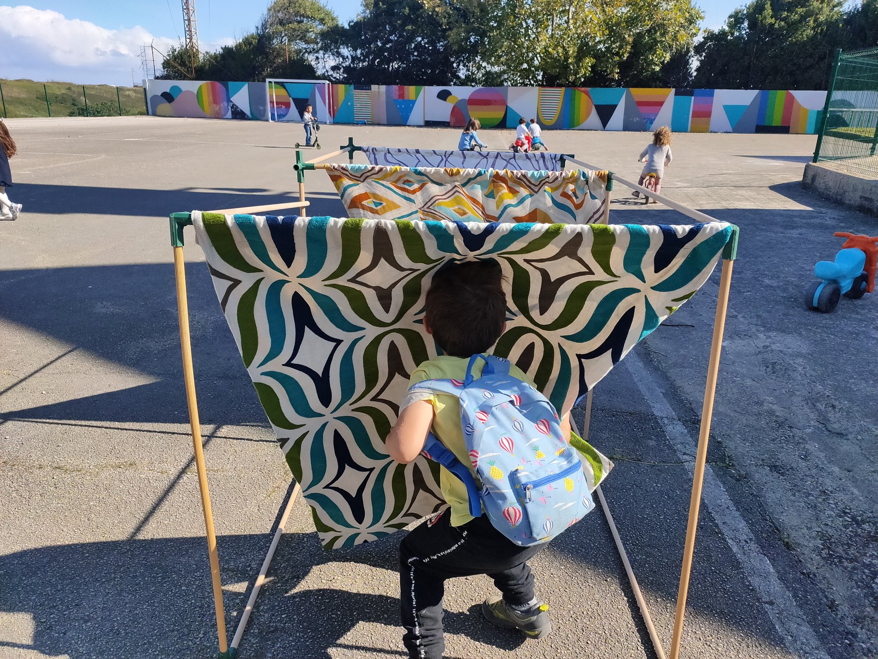 Niño atraviesa un refugio textil cúbico instalado en un patio escolar.