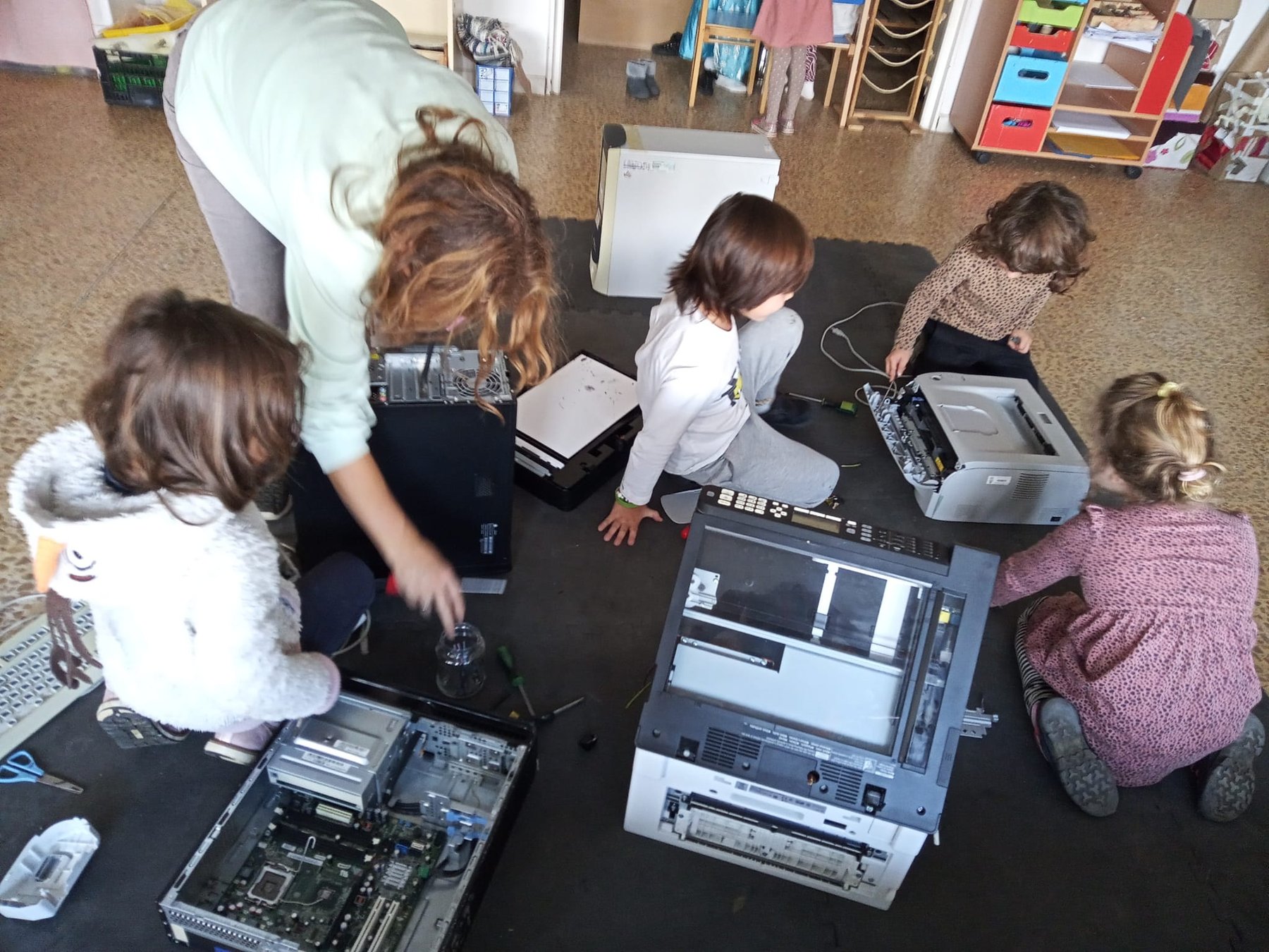Grupo infantil desmonta impresoras y ordenadores con acompañamiento adulto.