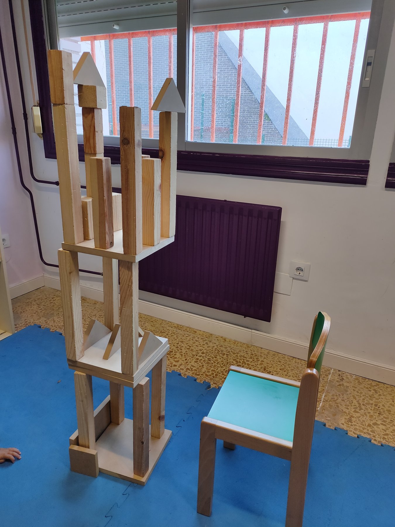 Estructura alta de listones y piezas triangulares construida junto a una ventana.