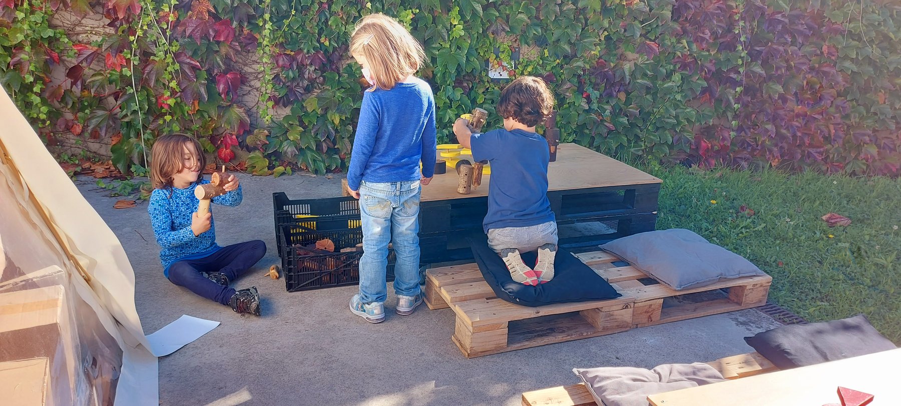 Tres niños combinan piezas geométricas en una mesa exterior.