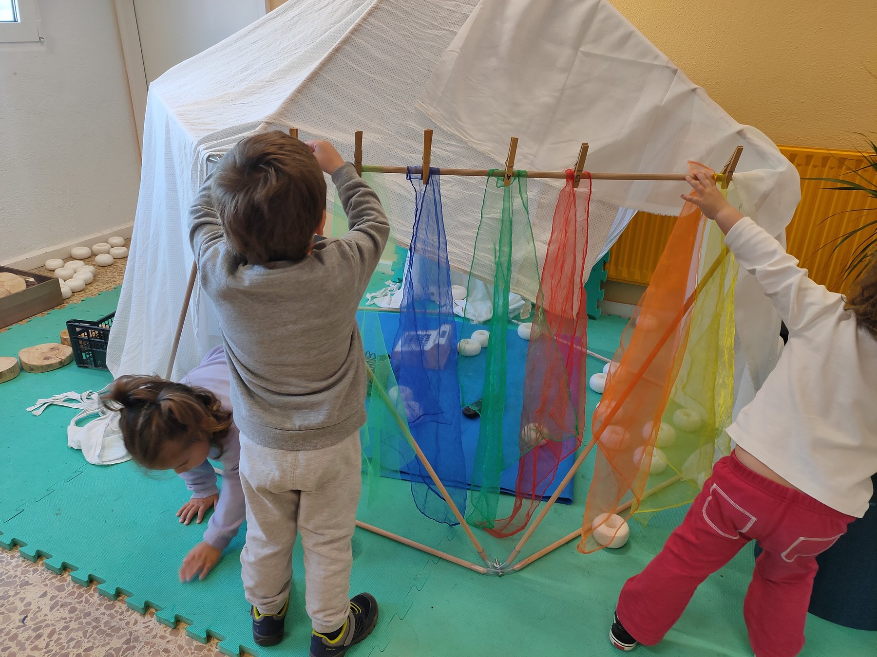 Niños pequeños modifican un refugio con telas translúcidas.