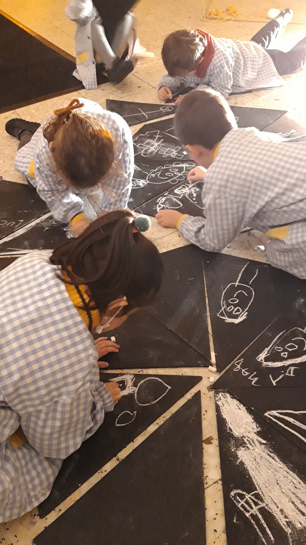 Grupo escolar dibuja colectivamente con tiza blanca.