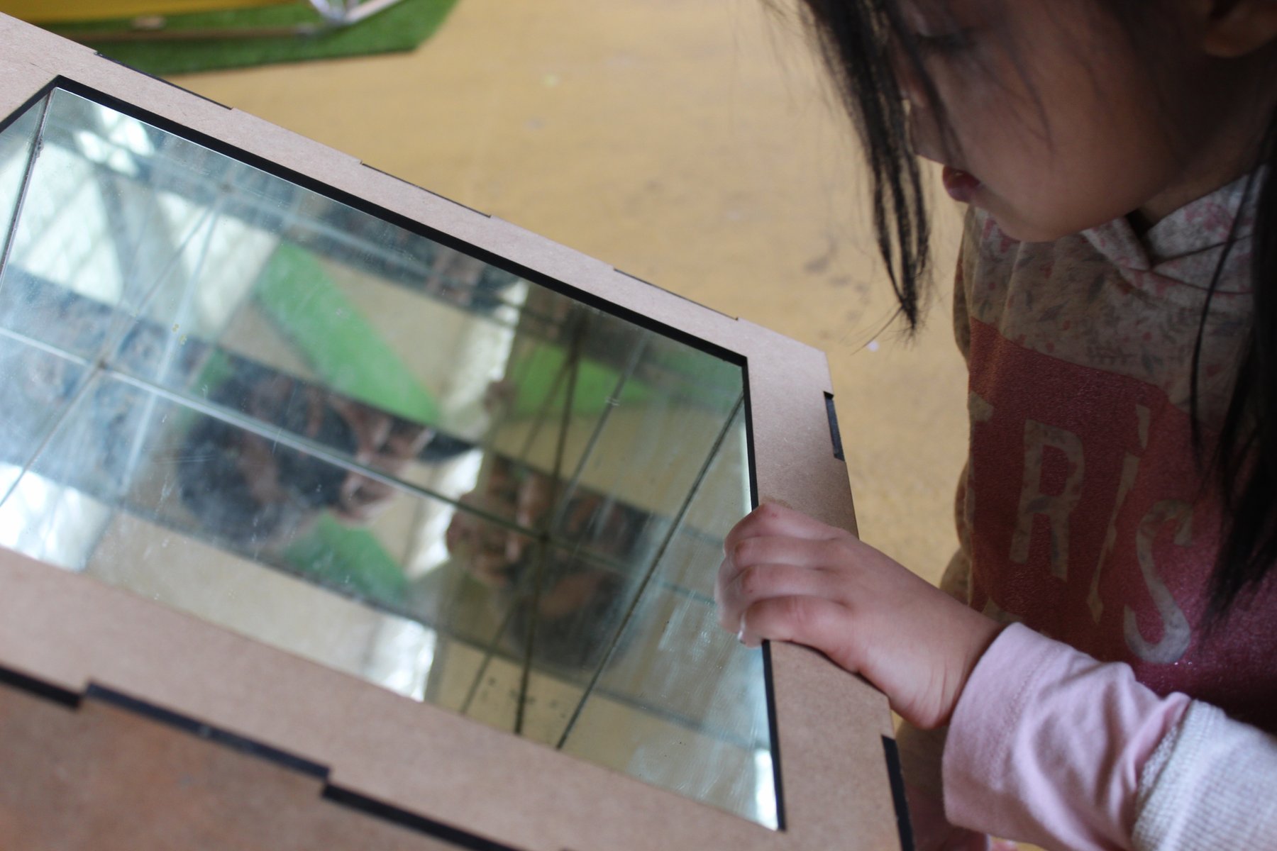 Una niña observa el interior de una caja de luz y espejos durante el taller Irisada.