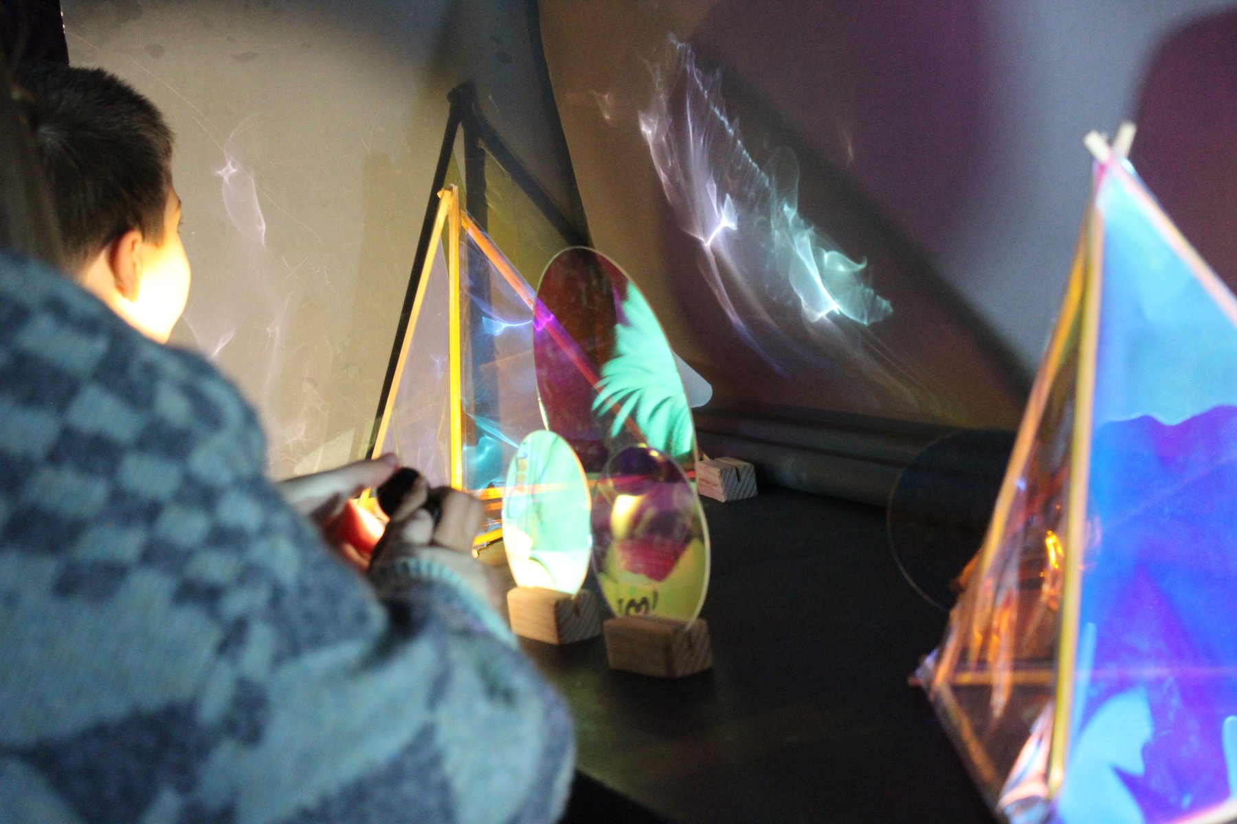 Niñas y niños experimentan con reflejos, transparencias y luz sobre una mesa.