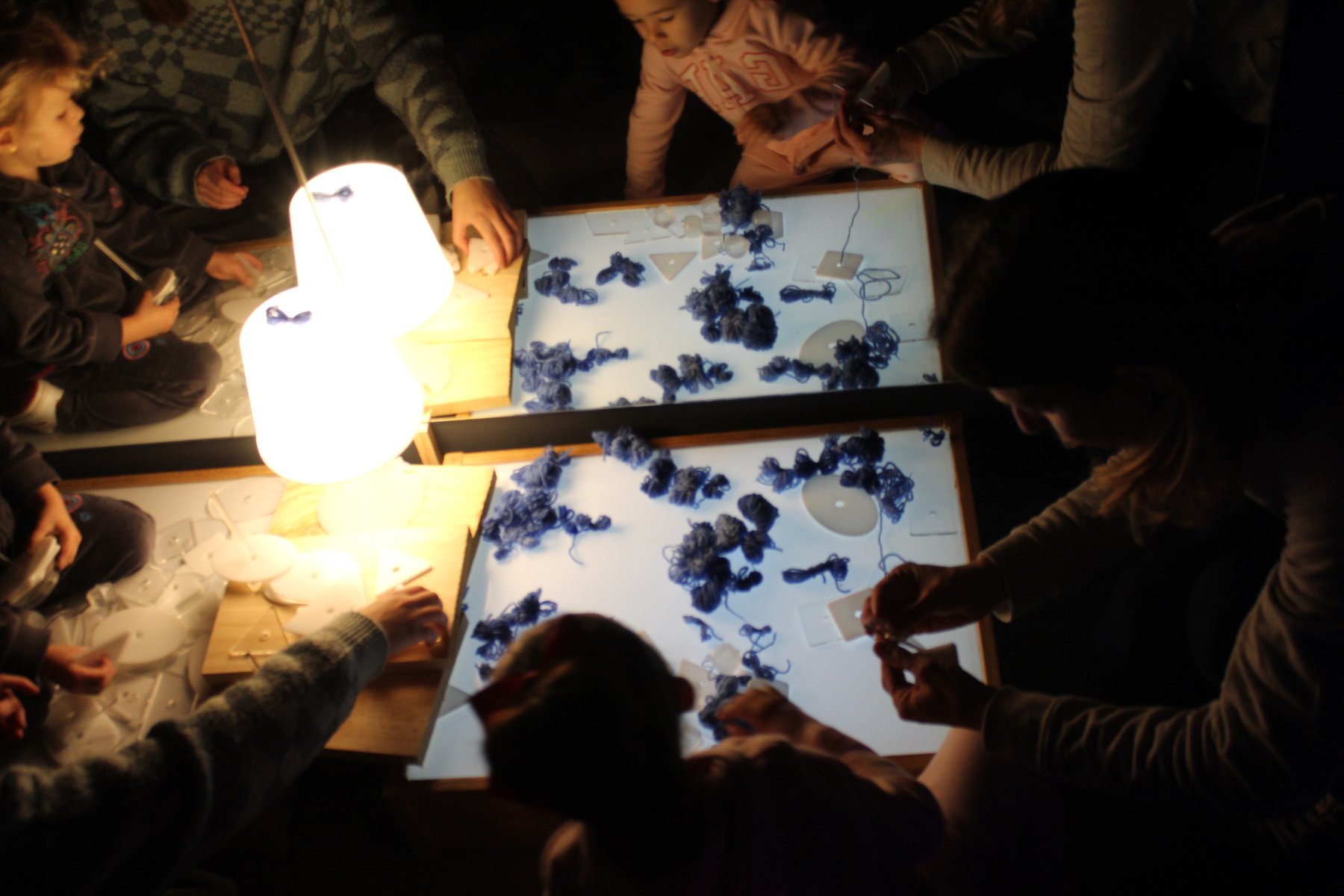 Niñas y niños trabajan juntos alrededor de mesas iluminadas en Caleidoscopio.