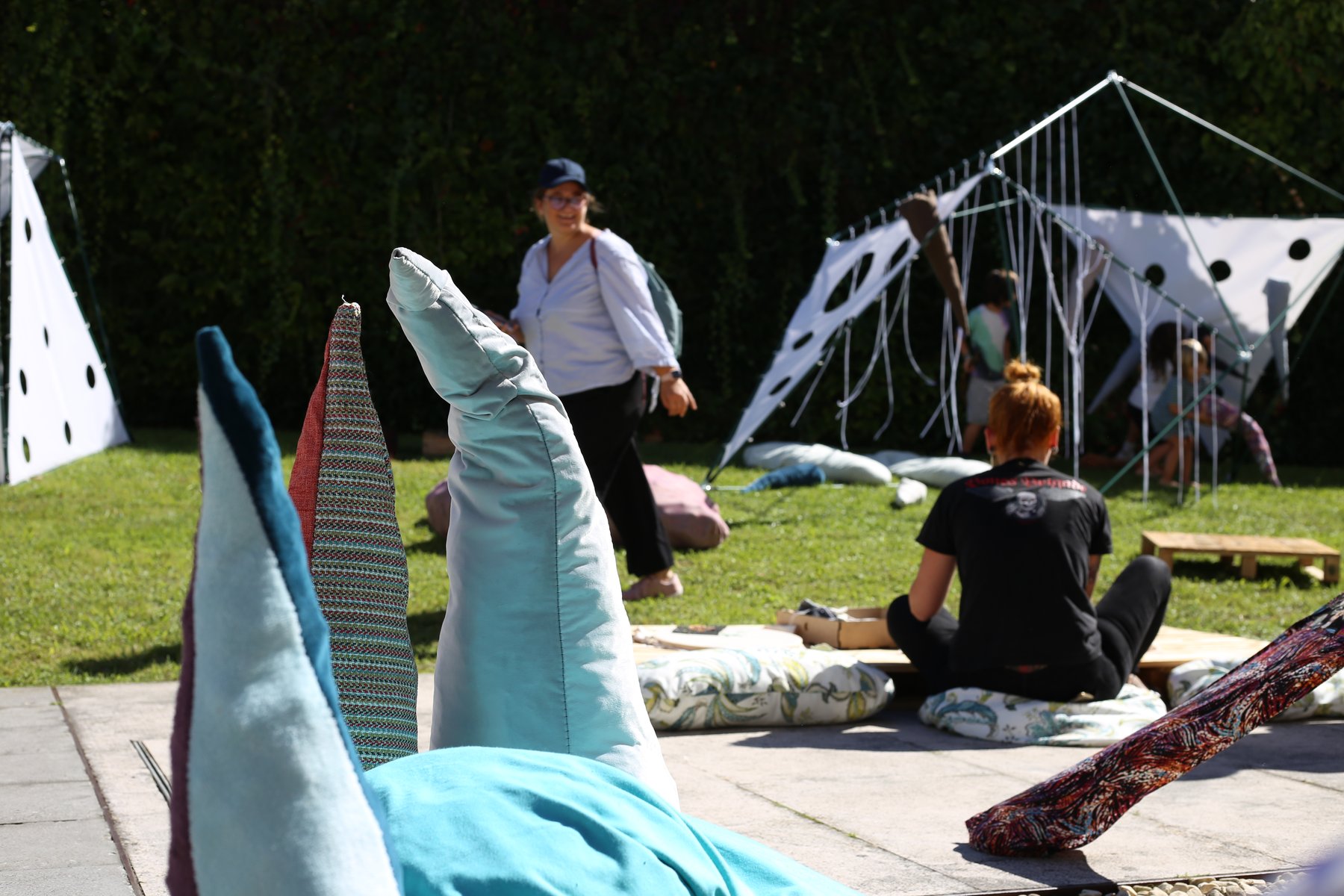 Formas textiles mullidas en primer plano y estructuras transformables ocupando el jardín.
