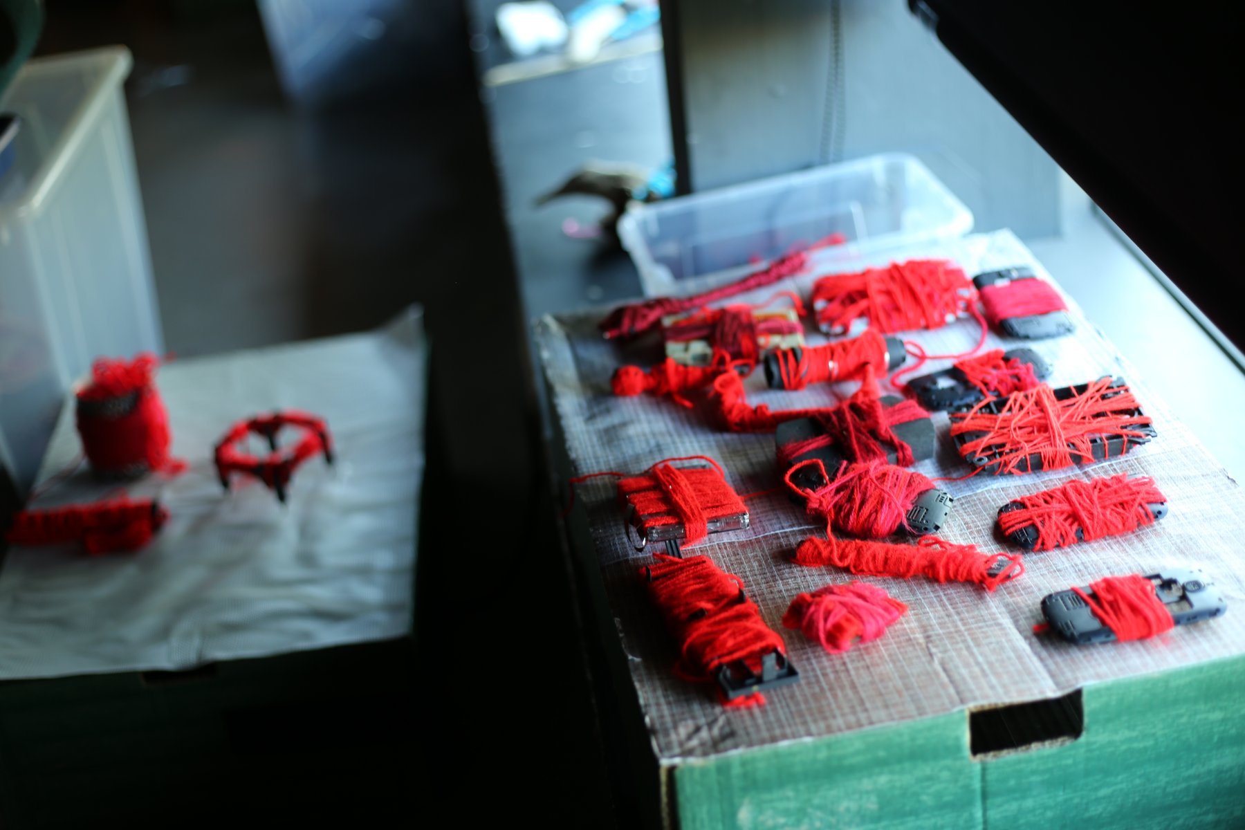 Pequeñas composiciones de hilo y tejido rojo dispuestas sobre una mesa de trabajo.
