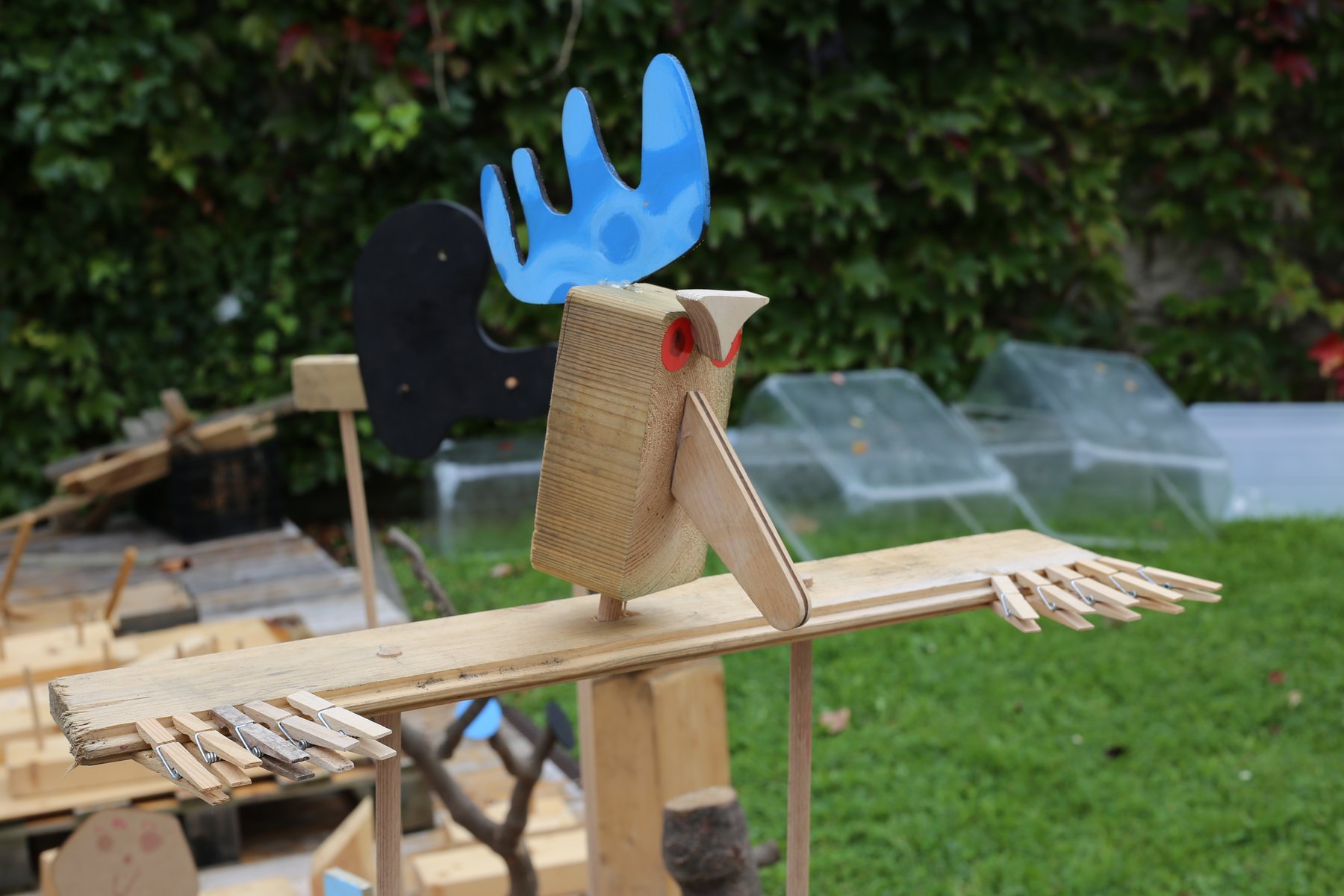 Personaje de madera con forma de ave integrado en el paisaje exterior.