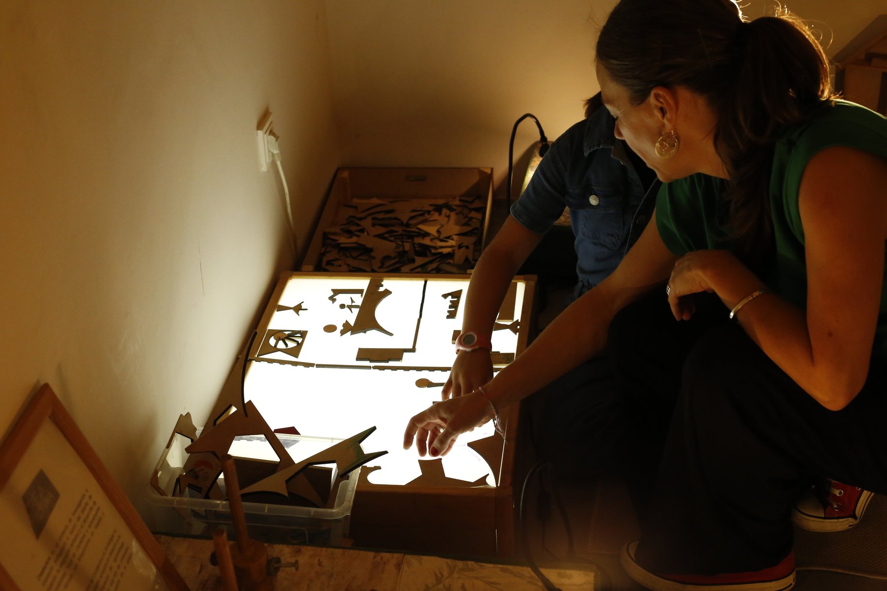 Una persona adulta acompaña la exploración de piezas de madera sobre una mesa de luz.
