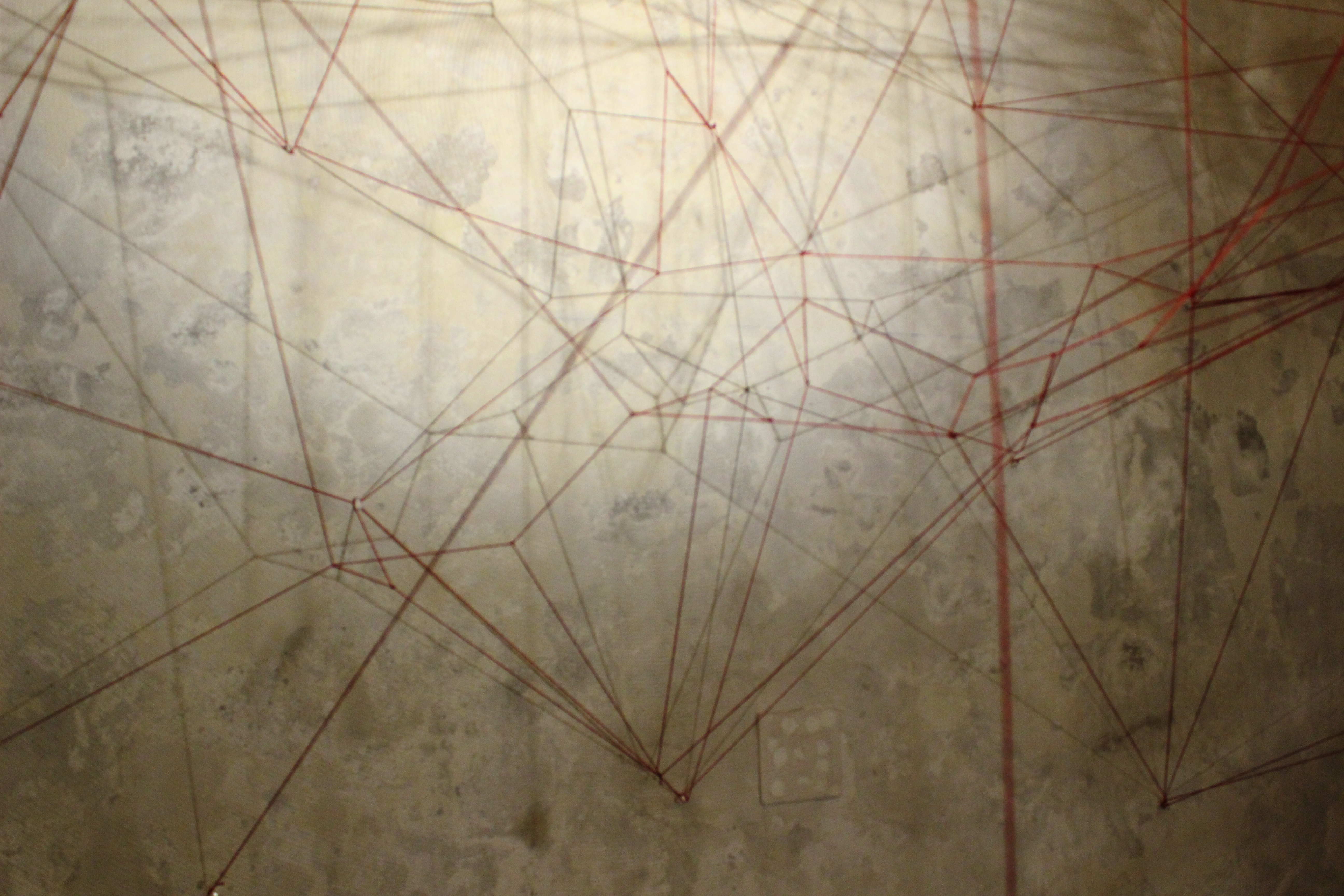 Dibujo expandido sobre la pared mediante hilos y pequeñas piezas.