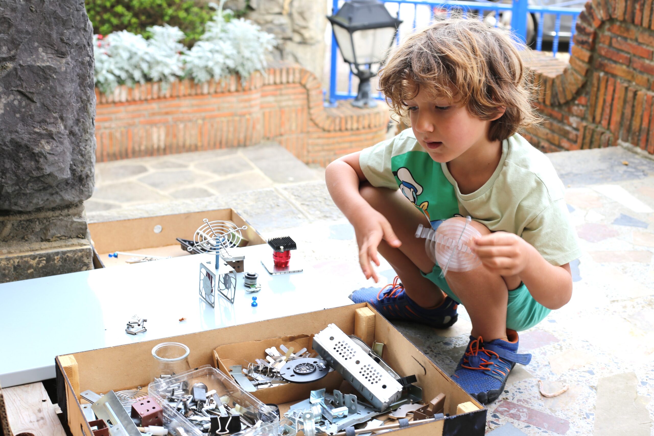 Un niño observa una pieza sobre una caja con componentes tecnológicos desmontados.