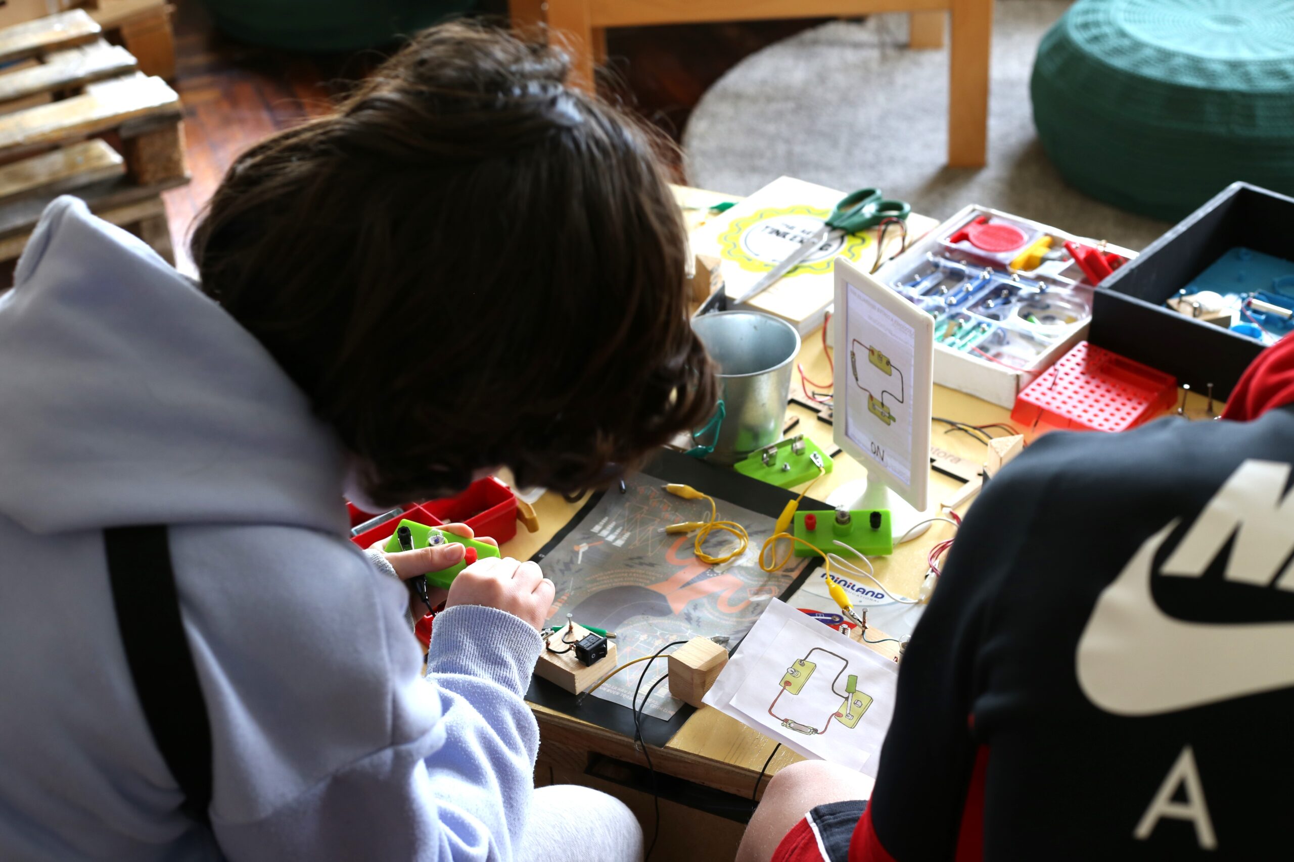 Participantes exploran una mesa con cables, pequeños componentes y materiales de montaje.